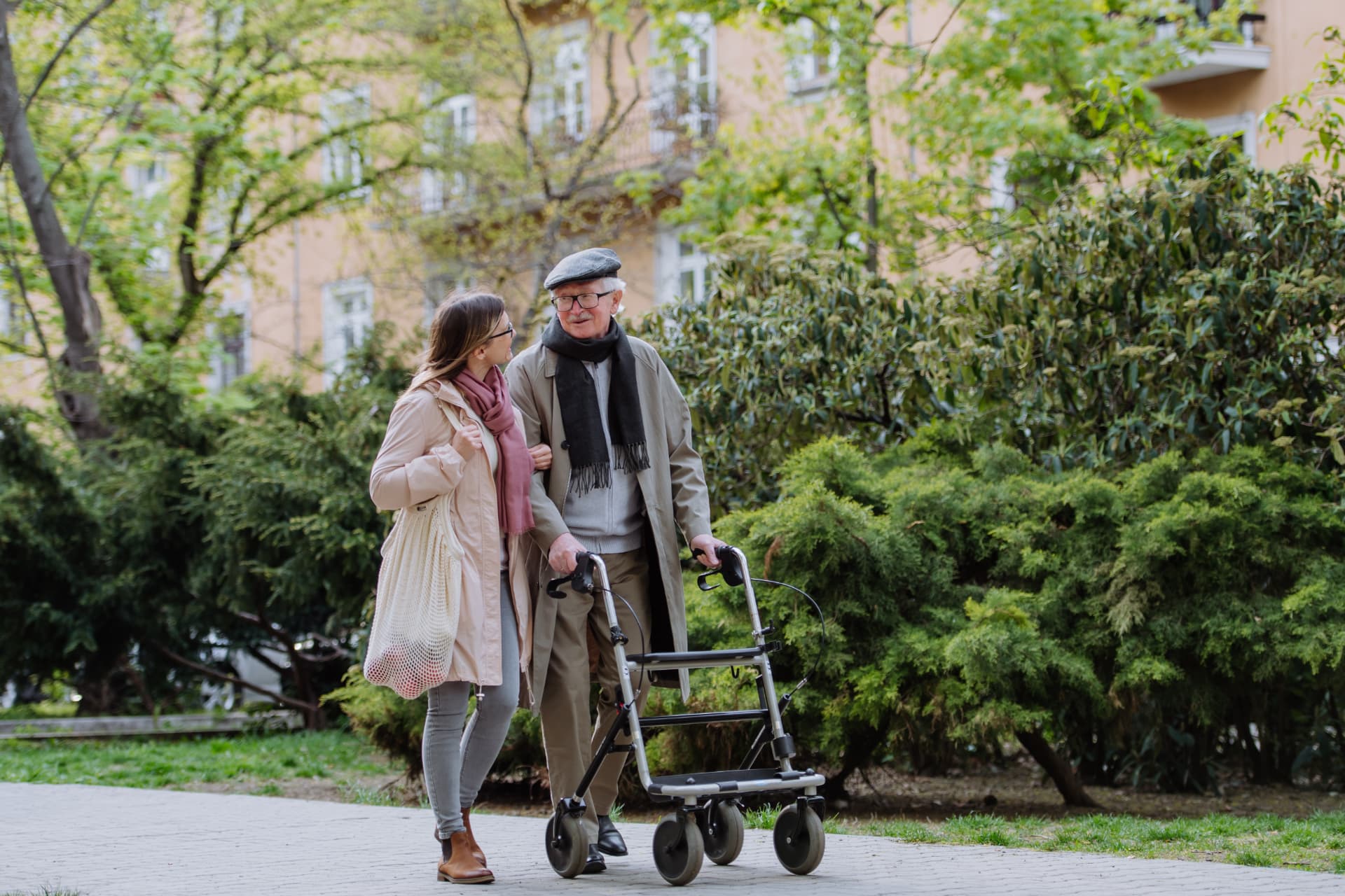 A woman walking alongside a senior man using his walker outdoors